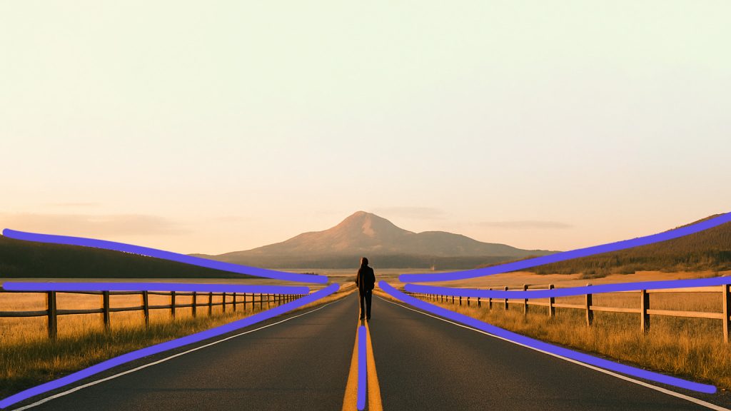 A person stands alone on a rural road at sunset, with wooden fences and road lines creating strong leading lines that draw the eye toward the horizon and distant hills.